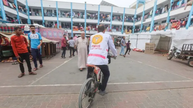 Dr. Hassan Zein Al-Din rides his bicycle inside a United Nations school where he will treat people displaced by the war. Despite being displaced from Gaza City due to the conflict, Dr. Hassan Zein al-Din, a 54-year-old Palestinian physician, cycles up to 15 kilometers daily, traveling through war-damaged areas, to provide medical care and follow-up check-ups for displaced individuals in shelter centers