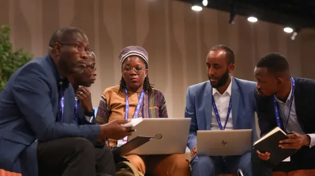 People in discussion gather around laptops in the COP28 summit in Dubai