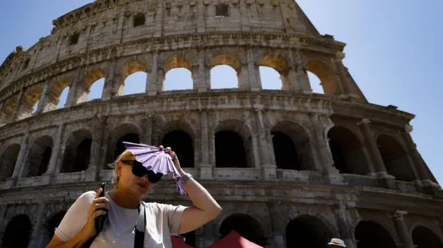 Tourist covers her head with a fan at the Colosseum in Rome, July 2023