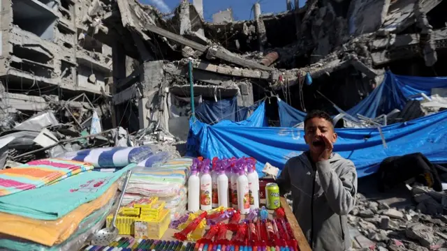 A Palestinian vendor offers his products in an open-air market near the ruins of houses and buildings destroyed in Israeli strikes during the conflict, amid a temporary truce between Hamas and Israel, in Nuseirat refugee camp in the central Gaza Strip November 30, 2023.