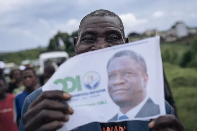 A supporter of Congolese doctor and presidential candidate Denis Mukwege holds a campaign poster at Kavumu-Bukavu airport, as Mukwege arrives for a campaign rally in Bukavu, capital of South Kivu province, eastern Democratic Republic of Congo