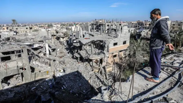 A man stands on a raised concrete platform overlooking destroyed buildings