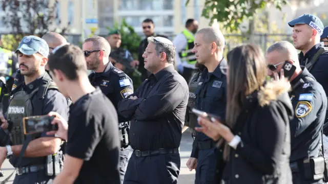 sraeli National Security Minister Itamar Ben Gvir (C) is escorted by security officials as he visits the area of a shooting attack at the entrance of Jerusalem, 30 November 2023.