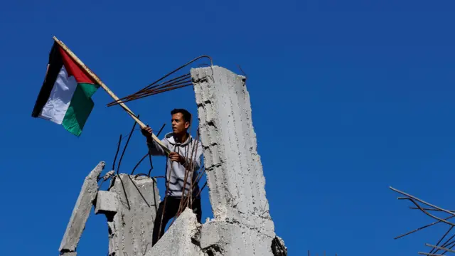 A man hangs a Palestinian flag on the ruins of his house destroyed by Israeli strikes during the conflict, 29 November