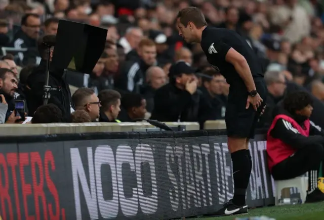 Referee John Brooks checks the pitchside monitor at Craven Cottage