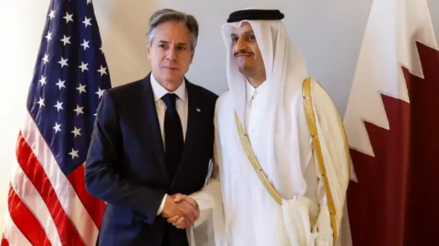 Blinken shakes hands with Qatari Prime Minister and Foreign Minister Mohammed bin Abdulrahman Al Thani in front of the American and Qatari flags