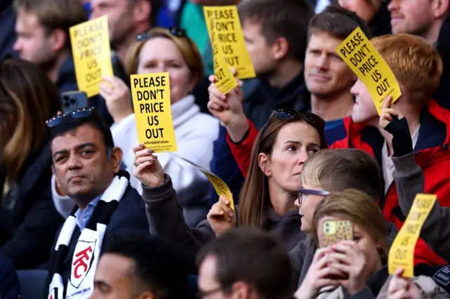 Fulham fans hold up a cards reading 'Please don't price us out [of the match]'