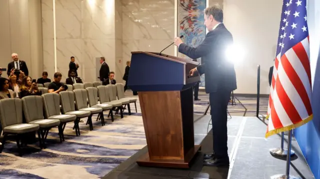 A photo of Blinken taken from behind as he speaks at a podium during a news conference