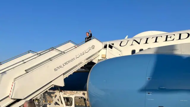 Antony Blinken waves from the steps of a plane