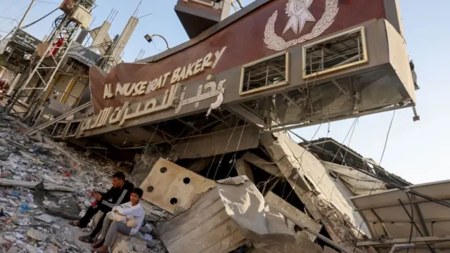 A Palestinian man and his son sit holding a bag of bread outside a destroyed bakery at the Nuseirat refugee camp in the central Gaza Strip on November 4, 2023