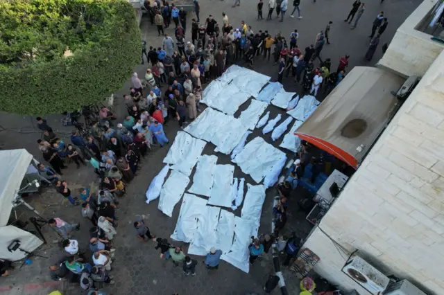 An aerial view of people gathered around white body bags at the Al-Aqsa hospital in Deir Al-Balah