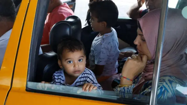 Palestinians, including foreign passport holders, wait at Rafah border crossing after evacuations were suspended on Sunday