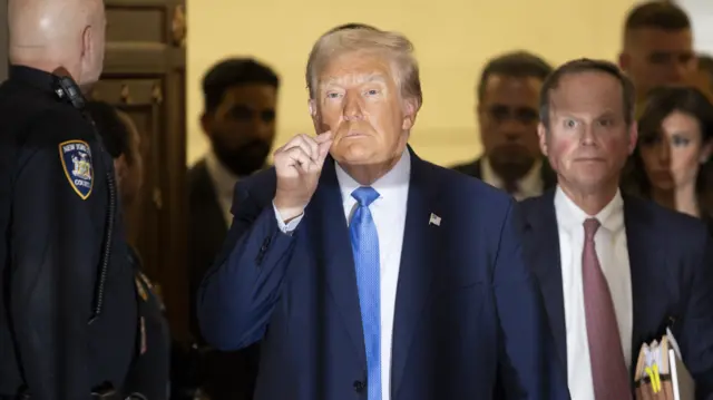 Donald Trump gesturing with his fingers together in front of his mouth as he enters the courtroom