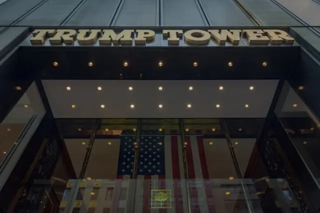 Trump Tower with the sign in light brown large lettering above the entrance. The camera is shooting from below, looking up at the building