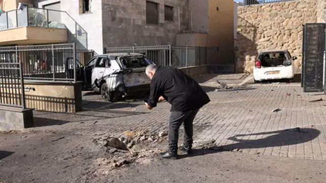 An Israeli man looks at a small crater and damaged vehicles the day after a rocket attack from southern Lebanon on the Israeli city of Kiryat Shmona in northern Israel