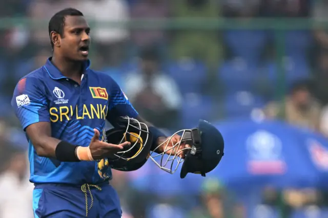 Angelo Mathews holding two helmets