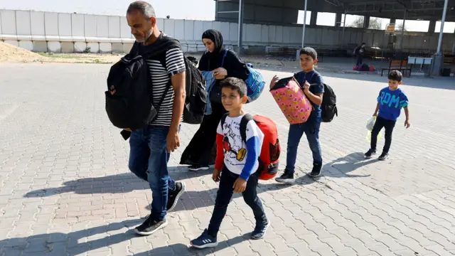 Family members carry their luggage as Palestinians, including foreign passport holders, wait at the Rafah border crossing to cross into Egypt