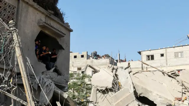 A group of Palestinians look out from a gaping hole in the ruins of a concrete building in Khan Younis