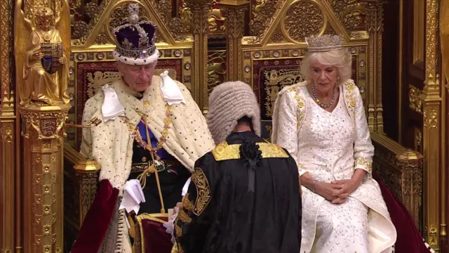 King's speech ends and King and Queen Consort, now sitting, led away