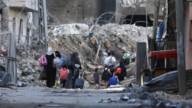 People walking with suitcases amongst piles of rubble in Gaza