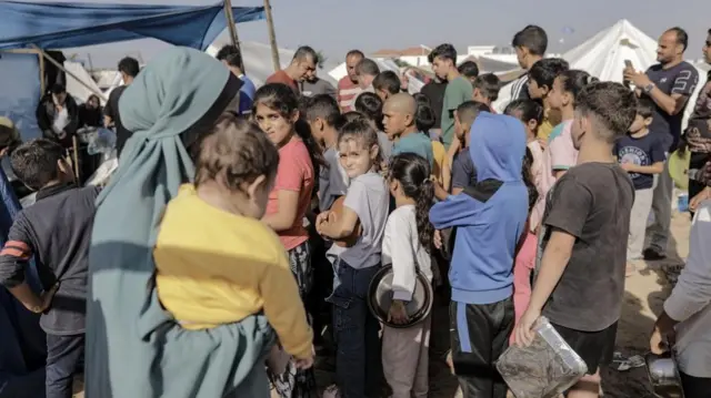 Palestinian children receive food between tents set up for Palestinians seeking refuge on the grounds of a United Nations Relief and Works Agency for Palestine Refugees (UNRWA) center in Khan Yunis refugee camp, west of the town of Khan Yunis, southern Gaza Strip, 25 October 2023.