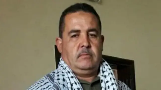 Mohammad Abu Hasira pictured wearing a keffiyeh around his shoulders. He is a middle aged man with a serious look on his face.