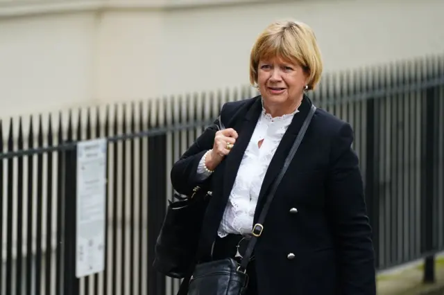 Baroness Heather Hallett walking past an iron fence with a handbag on her shoulder