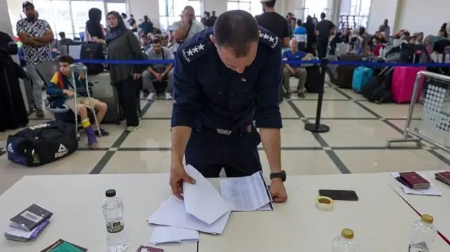 A Palestinian border guard checks the documents of dual nationals and foreigners as they wait to cross the Rafah border crossing