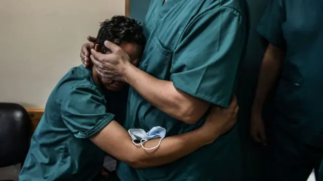 One man in medical scrubs is comforted by another in medical scrubs