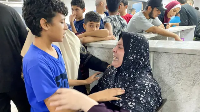 Young boy stands next to woman as she cries at Al Shifa hospital