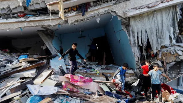 Young boys clamber through the rubble of a partially collapsed building, Khan Younis