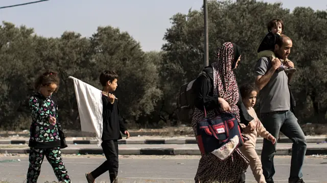 A family flees, with a man carrying a child on his shoulders