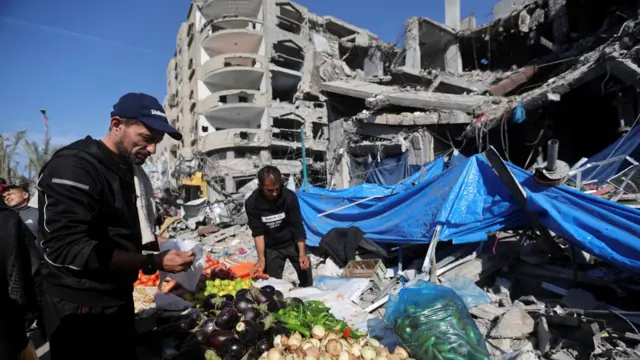 A Palestinian vendor prepares his products in an open-air market near the ruins of houses and buildings destroyed in the war between Hamas and Israel