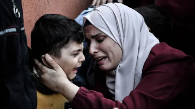 A woman holds the face of a young boy as they both cry