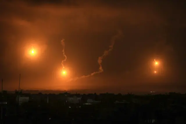 A night-time scene in which buildings are lit up by three yellow flares