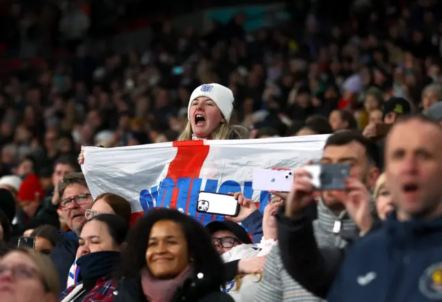 A fan holds a flag up and screams support from her seat.