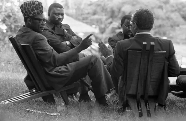 Presidential Residence - Kinshasa, Zaire Ð Secretary of State Henry A. Kissinger, President Mobutu Sesi Seko, Others Ð seated in circle on lawn chairs, talking; Henry KissingerÕs back to camera; Mobutu wearing leopard skin hat Ð Kissinger