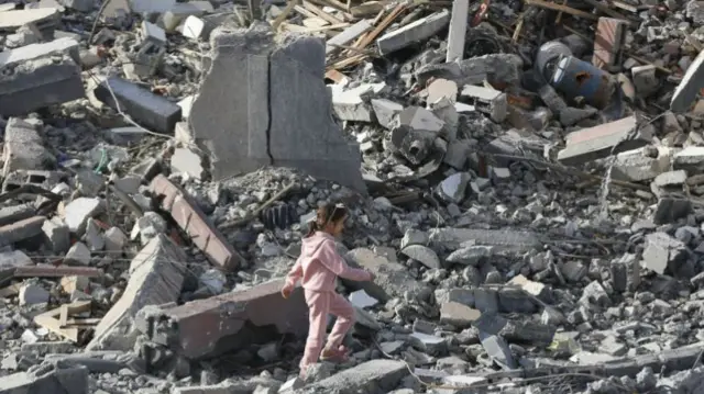 A young girl walks across an enormous pile of rubble