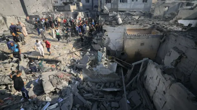 A crowd stands round an enormous pile of rubble