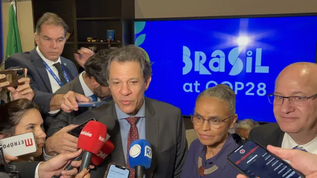 Fernando Haddad and Environment Minister Marina Silva speak to a gaggle of reporters with microphones