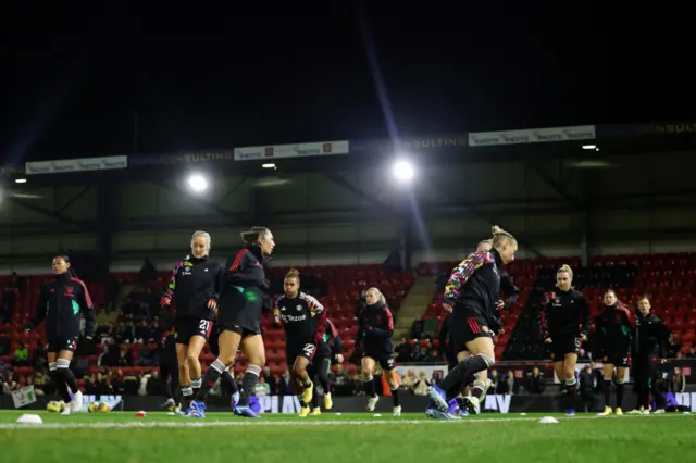 The Man Utd squad warm up under the lights at Brisbane Road.