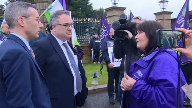 Stephen Farry and Andrew Muir speak to protesters outside Hillsborough Castle