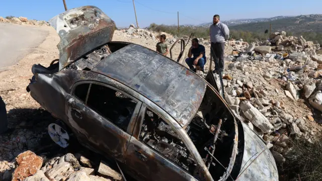 Palestinians inspect a car burnt by Israeli settlers earlier this month at Qarawa village in the West Bank