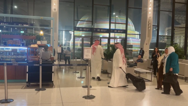 Two men and two women walk past cafe inside hall, dark outside.