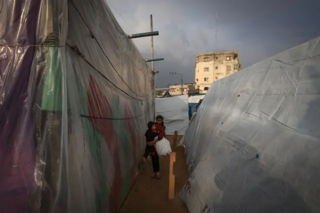 A Palestinian girl carries a child at camp for displaced people in Rafah