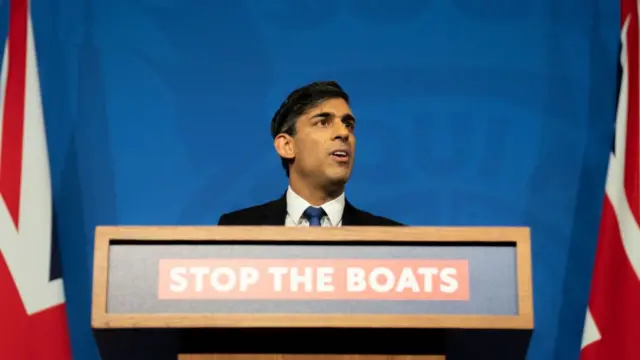 Rishi Sunak in front of a podium reading 'stop the boats'