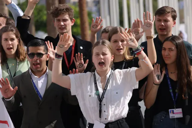 Demonstrators at COP28 hold up their hands in protest