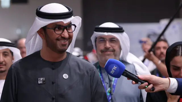 Sultan al-Jaber smiles as a journalist holds out a microphone to him at COP28