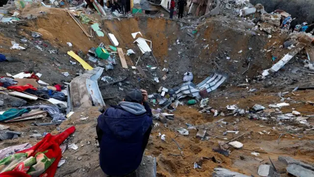 A man crouched in front of a massive crater filled with debris