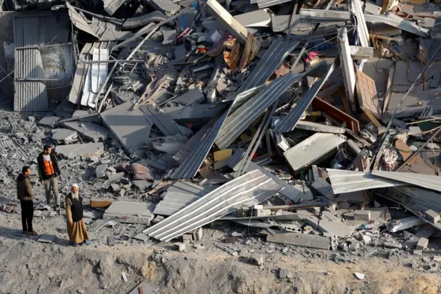 Palestinians look at debris at the site of Israeli strikes on homes